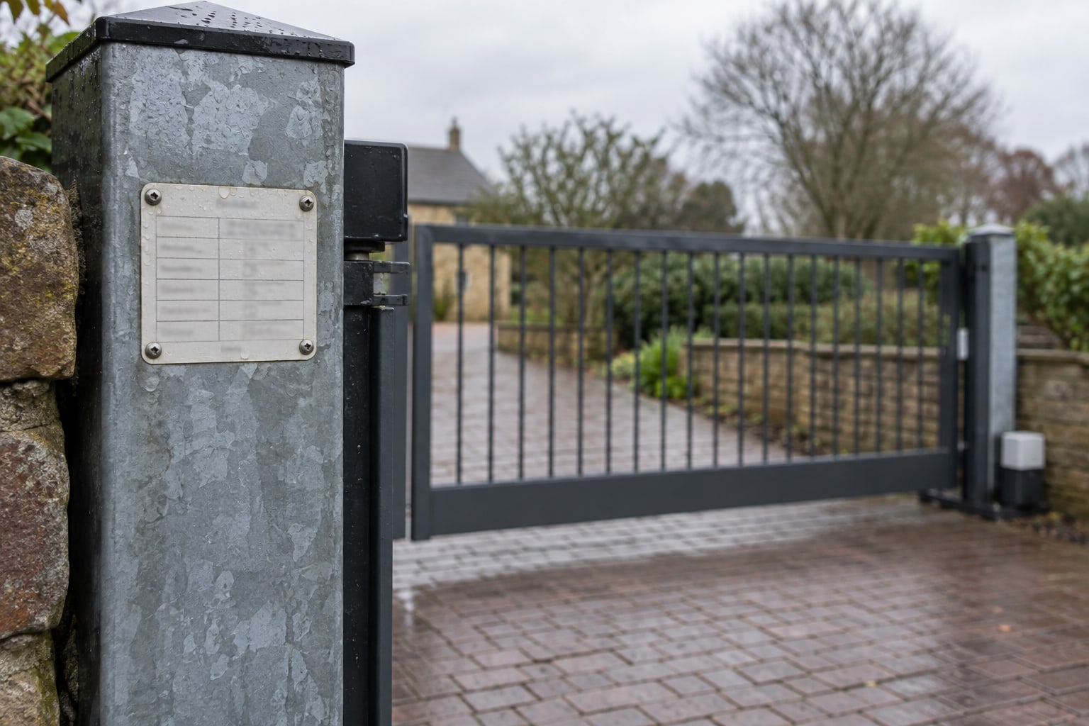 A small weatherproof service label is fixed to a gate post beside a driveway.